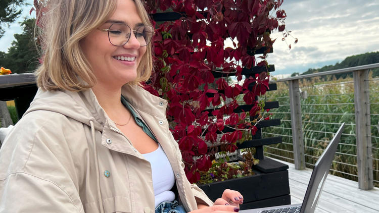 Julia på Lexicon Interactive med dator i knät utomhus med höströda löv bakom