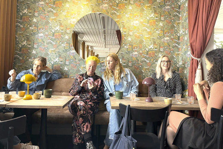Fyra glada tjejer på Lexicon Interactive vis fikabord framför blommig tapet