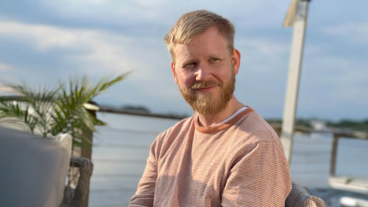 Anton på Lexicon Interactive sitter i solen med en sjö i bakgrunden