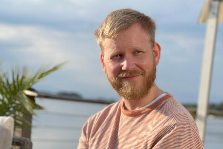 Anton på Lexicon Interactive sitter i solen med en sjö i bakgrunden