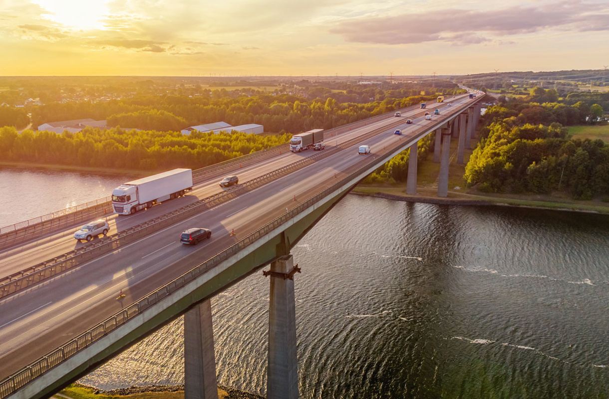 Bro med lastbilar och biltrafik i solnedgång