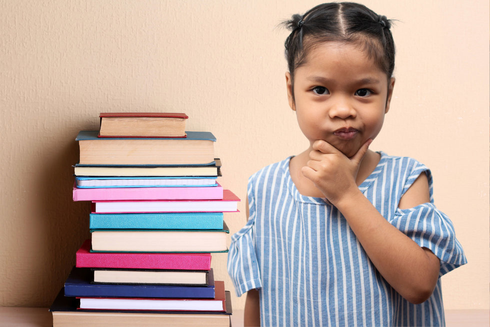 En flicka ser fundersam ut vid en trave böcker