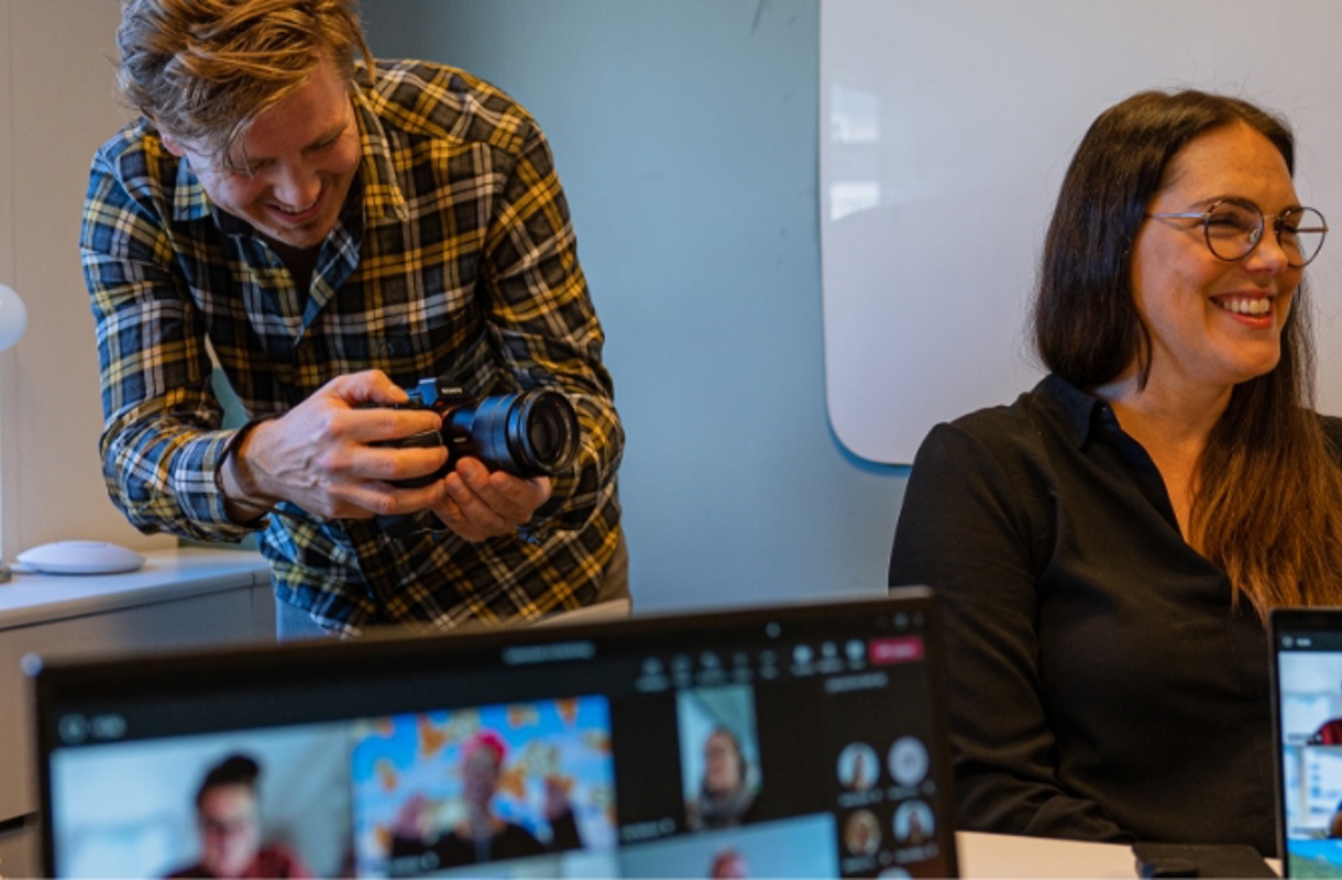 Skärmar visar teamsmöte och bakom står en fotograf och glad tjej