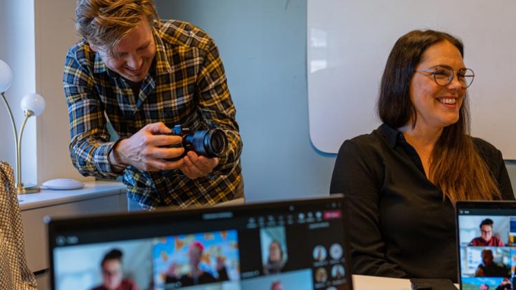 Skärmar visar teamsmöte och bakom står en fotograf och glad tjej