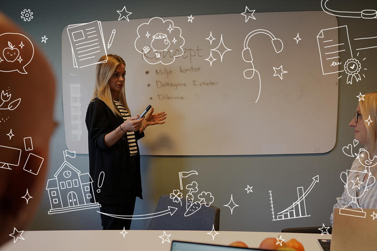 En presentatörer står vid en whiteboard under ett möte. På tavlan är det skrivet Koncept