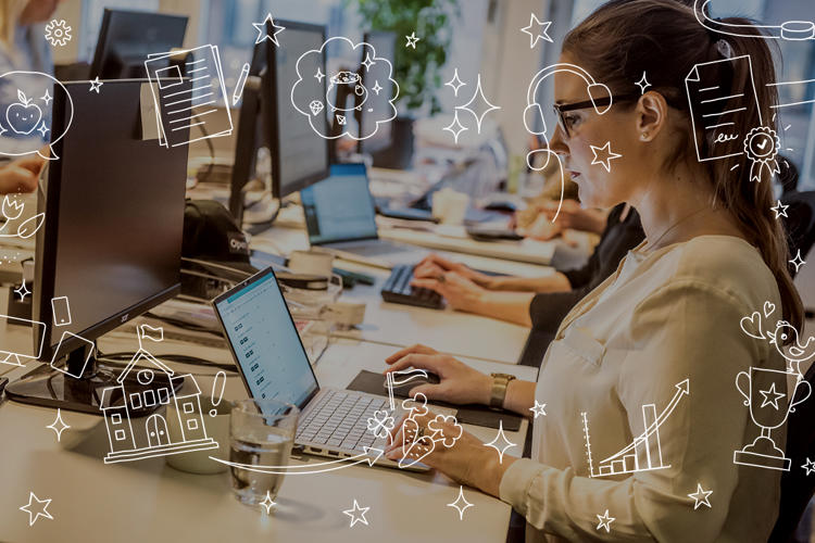 En skrivbordsrad med folk som jobbar vid sina datorer. Tjej med hästsvans och glasögon i förgrunden