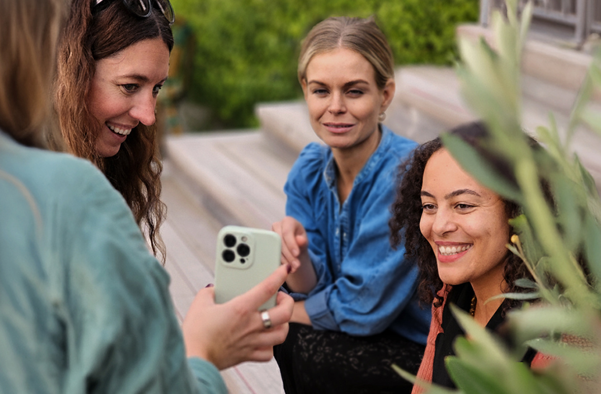 Flera tjejer på en trätrappa utomhus tittar i en telefon